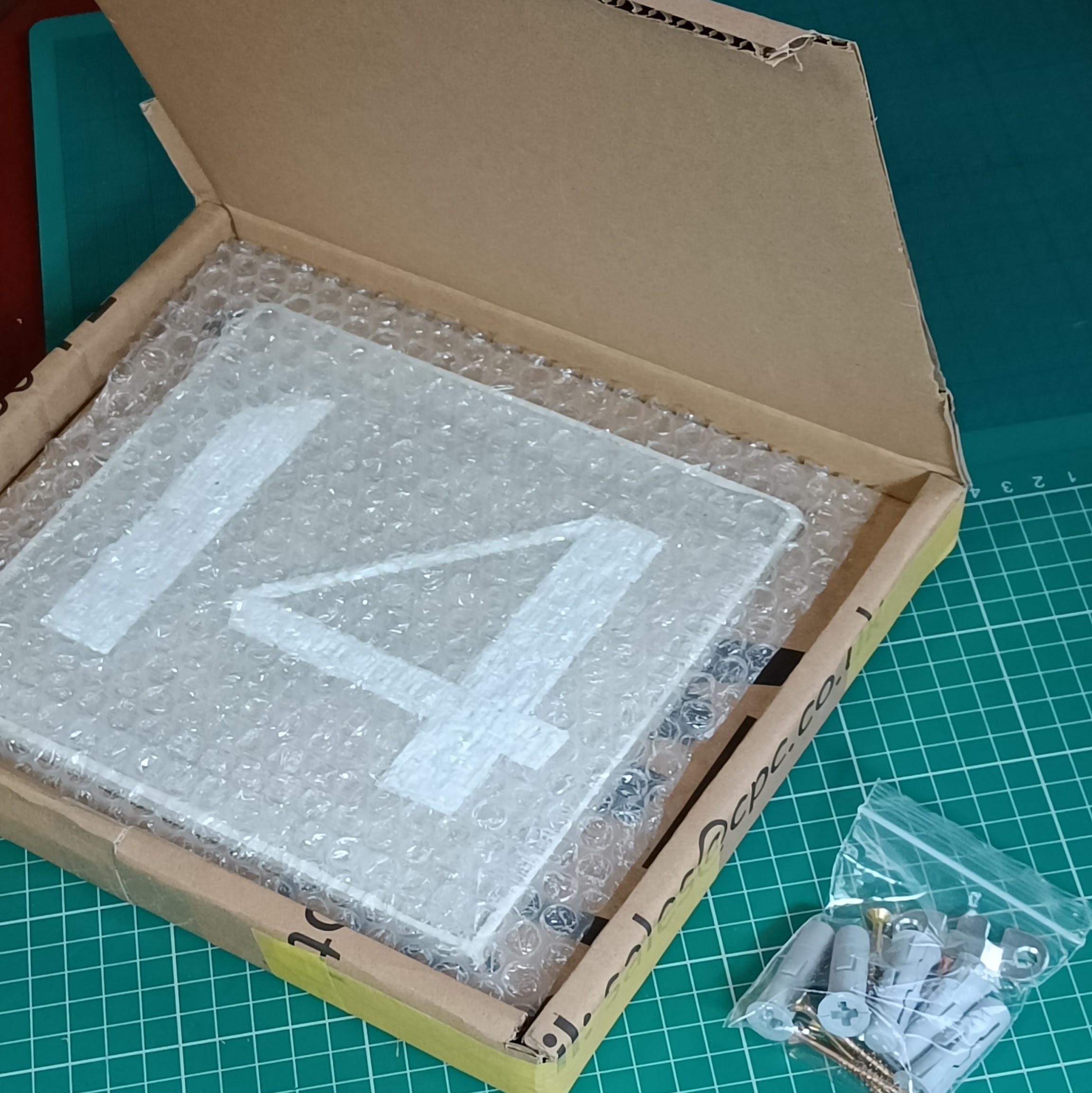 A homemade cardboard box with a concrete plaque resting
  inside, covered with a piece of bubblewrap. Nearby lies a
  little ziploc bag with some screws and 10mm rawl plugs in.