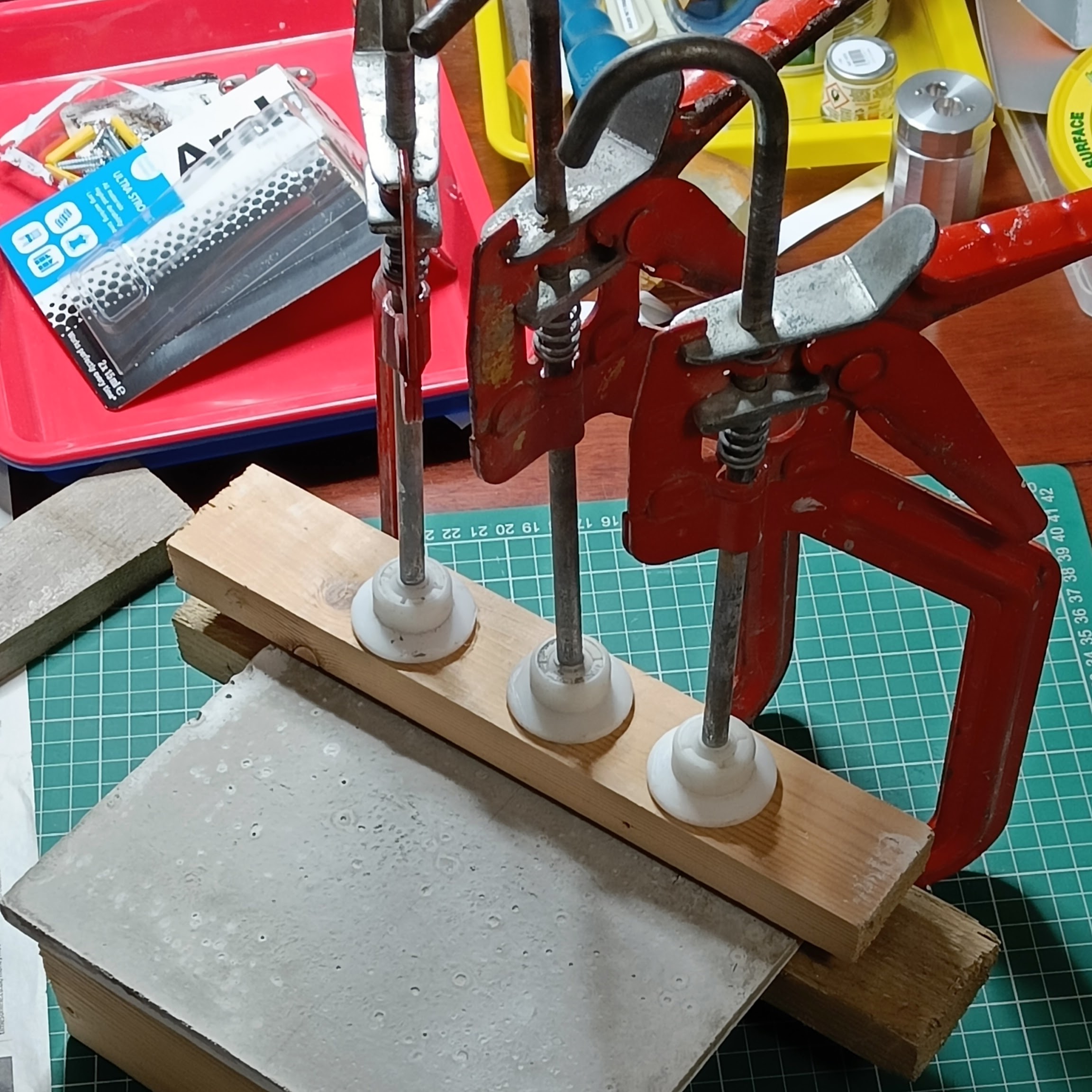 Three red metal clamps sit on my untidy desk and hold the
  concrete plaque in place between two pieces of wood. You can’t
  see the metal mounting plates that are being glued to the
  concrete plaque.