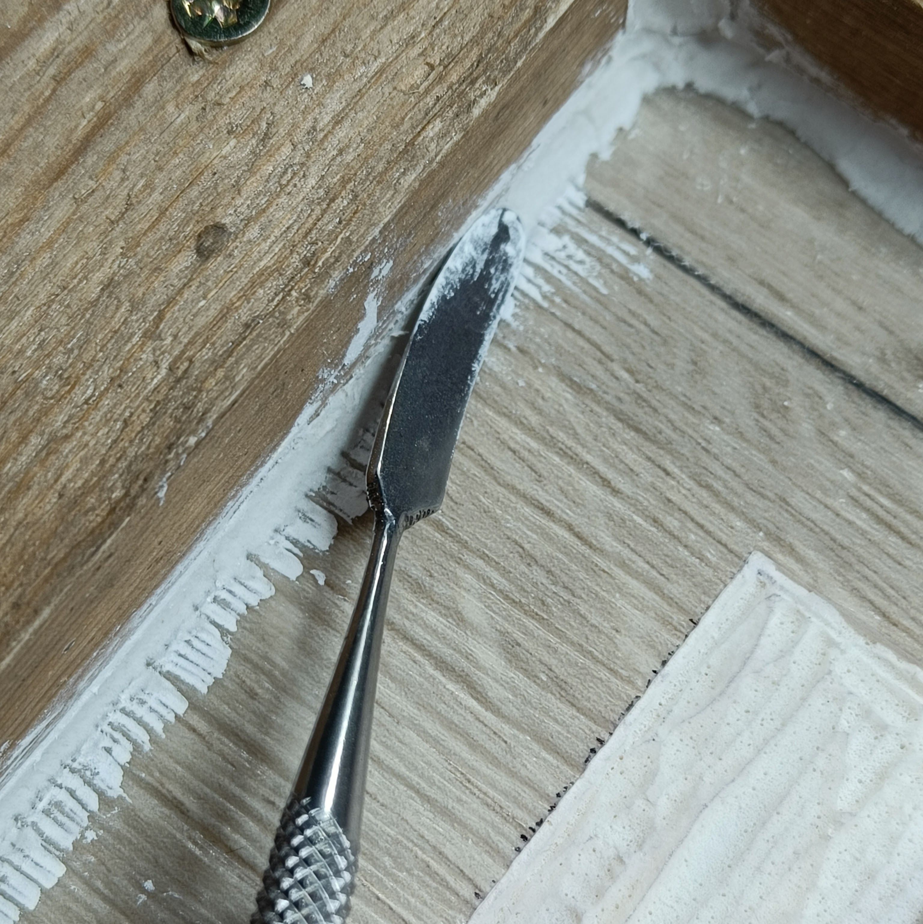 a close up of where the vinyl meets the edge of the
  frame. Modelling clay has been somewhat messily pressed into
  the edge, and a metal tool with an elongated spatulate
  business-end is pressed into the clay.