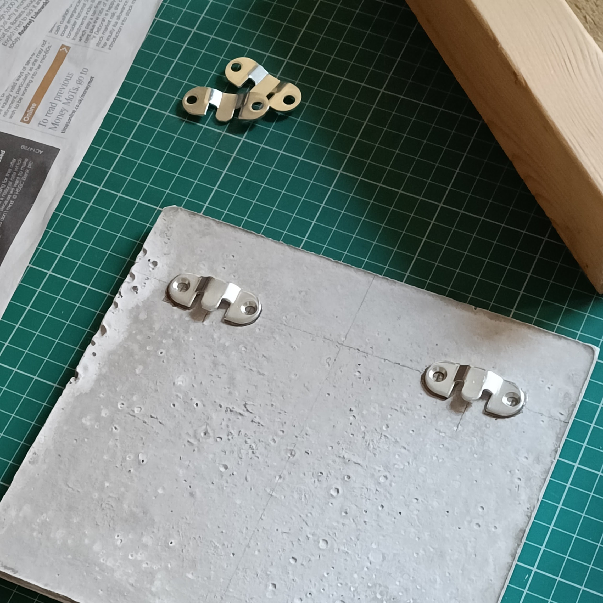 two metal mounting plates are glued to the back of the
  concrete plaque. Lying off to one side are the two other
  mounting plates that are identical and will eventually be
  screwed into the wall to support the plaque.