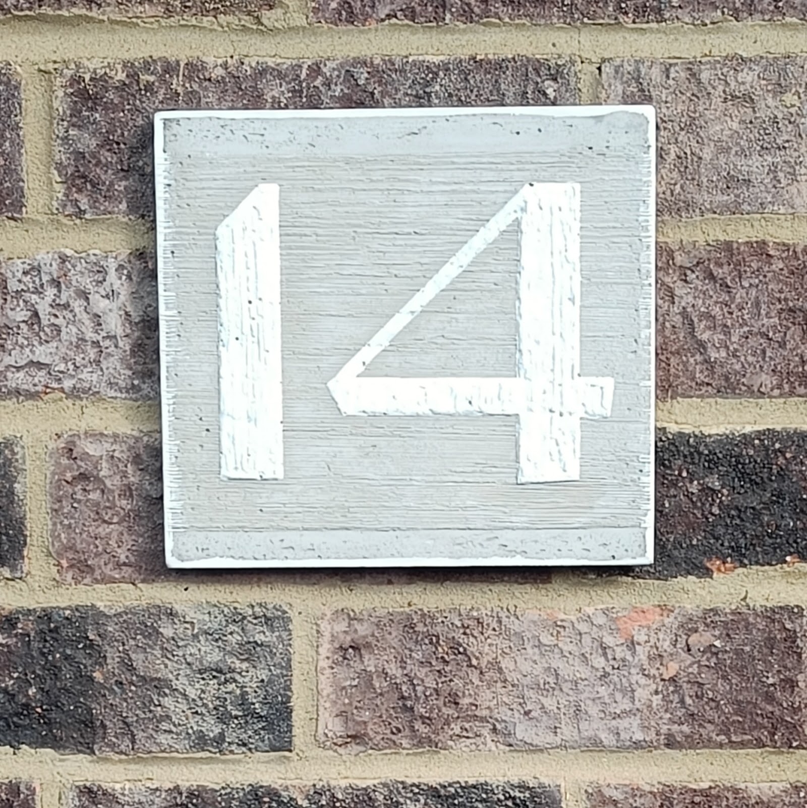 a concrete plaque on a brick wall; the number 14 is
  painted white on the concrete plaque and is raised up a little
  from the surface