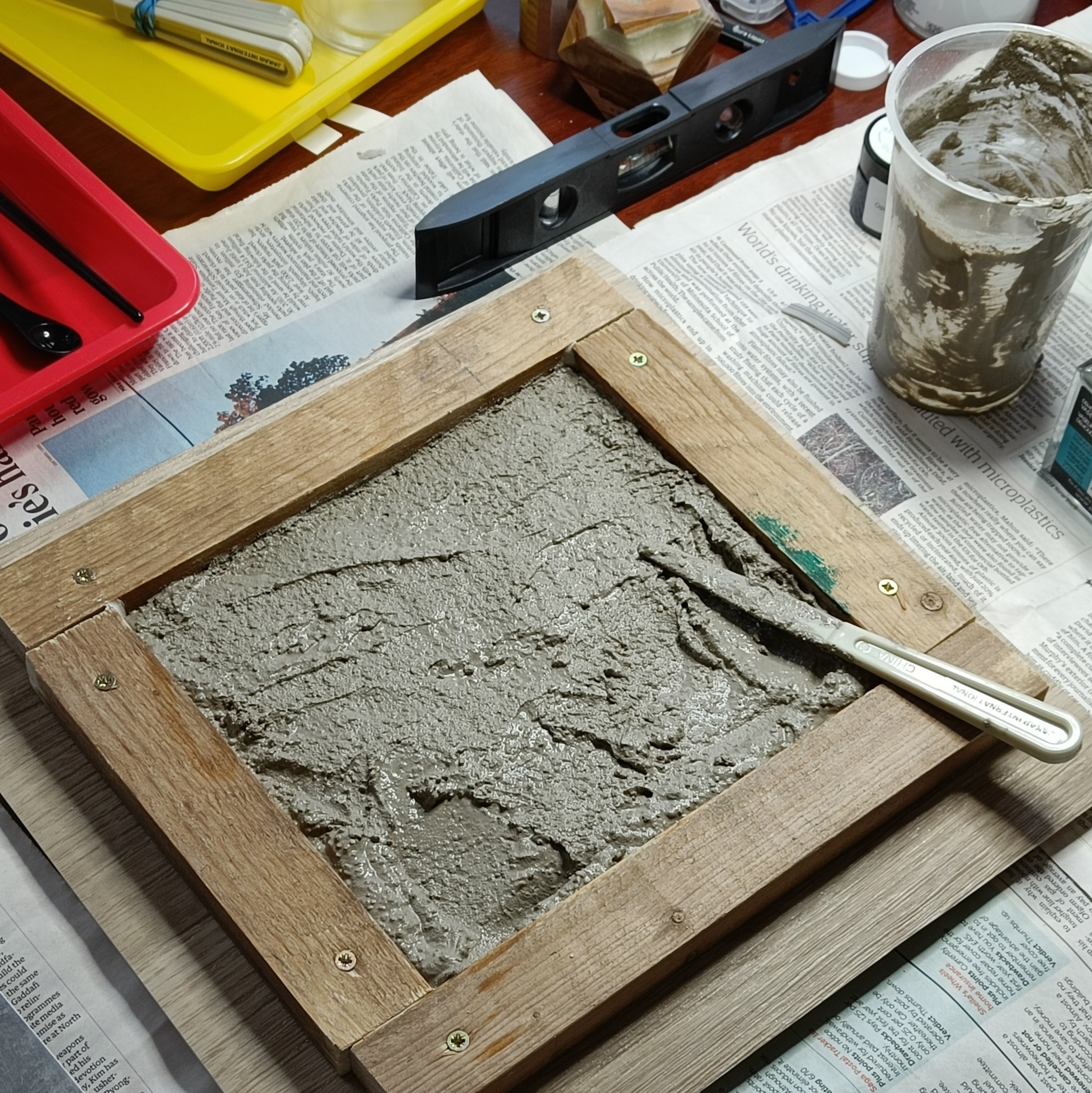the mixed concrete has been poured and scraped into the
  frame, and roughly levelled with the entirely inadequate
  plastic palette knife meant for inking