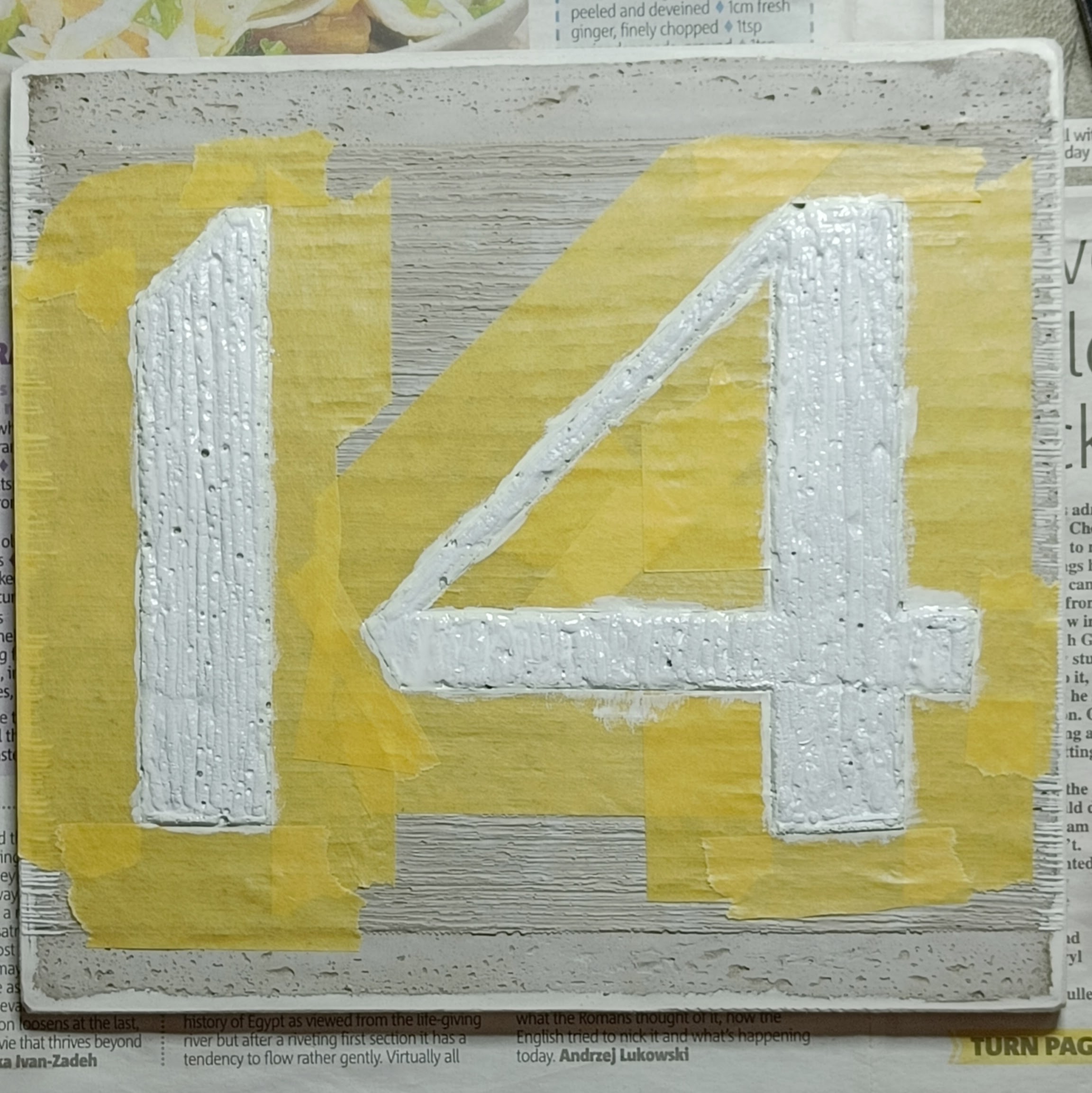 a concrete plaque showing a number 14. Around the figures
  and inside the counter i have carefully taped using Frogtape
  yellow. The numbers are painted white, mostly keeping to the
  lines, and only a little bit on the tape.